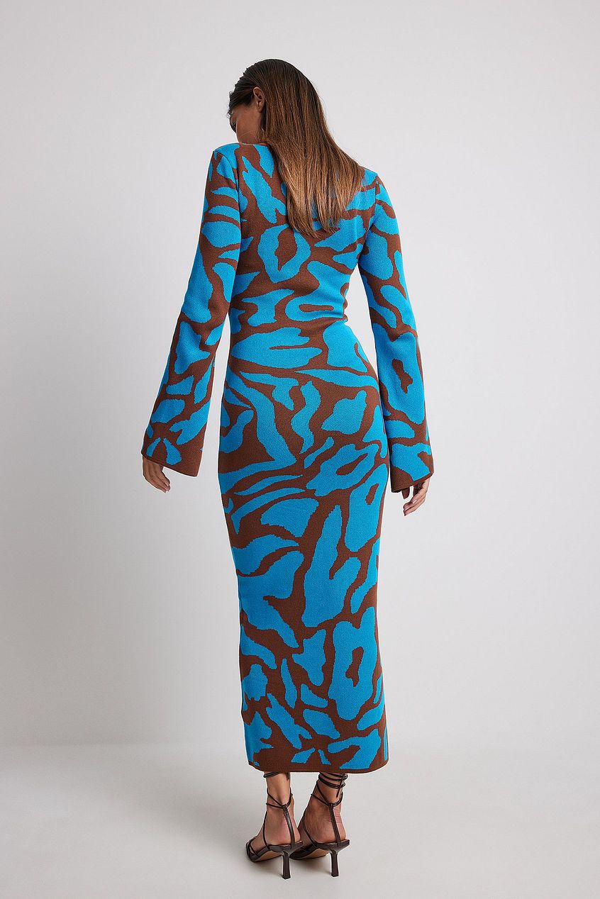 A woman models a long-sleeve, crewneck bodycon maxi dress featuring a bold abstract animal print in bright blue and brown. She is walking forward against a plain light grey background, wearing black strappy high heels.