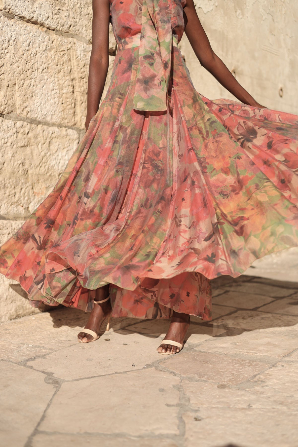 Flower - A model walking outdoors wearing a flowing, floral chiffon maxi dress featuring a halter neckline with an oversized bow and a banded waist.