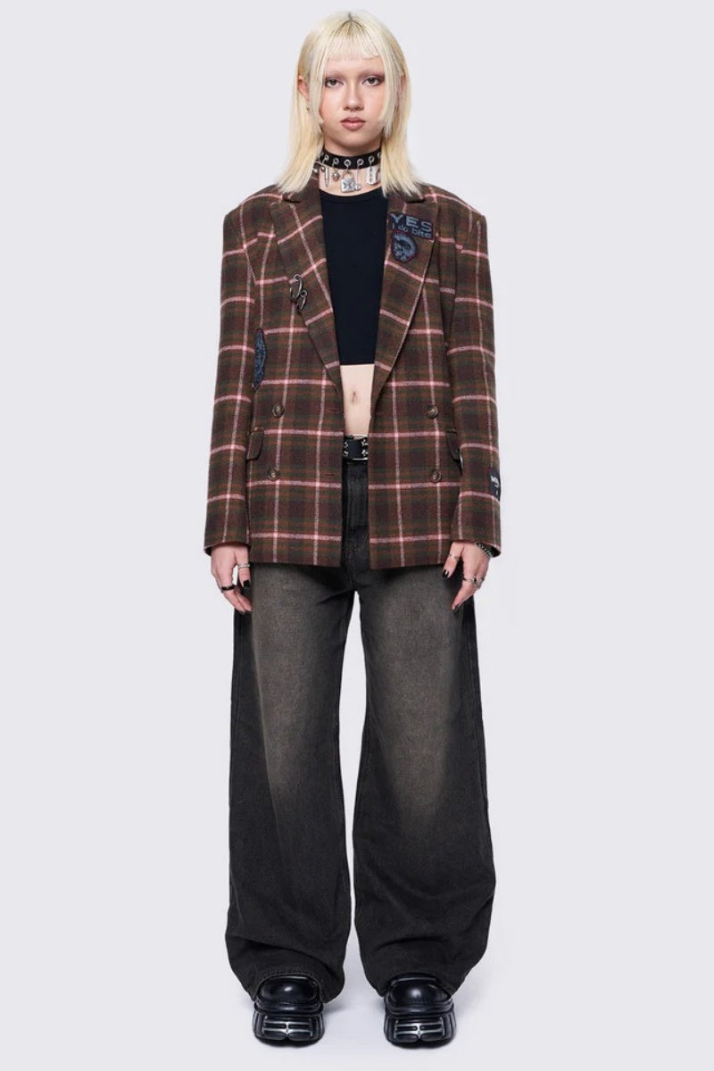 Brown - A woman wearing an oversized brown and pink plaid double-breasted blazer featuring edgy graphic patches and metal hardware details, styled over a black crop top.