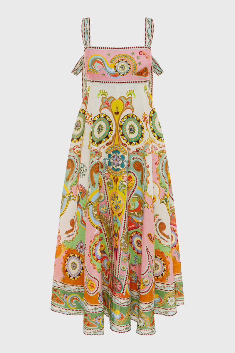 Multicolor - A model wearing a linen midi dress with a colorful kaleidoscope print, featuring a square neckline, wide straps, and an A-line skirt, standing next to a vintage pinball machine.