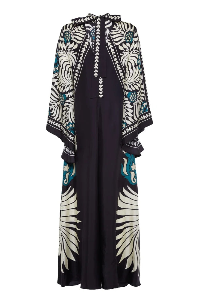 Multi - A woman wearing a high-neck maxi dress featuring a bold black, cream, and teal botanical medallion print, designed with dramatic cape sleeves and a fluid, floor-length skirt.