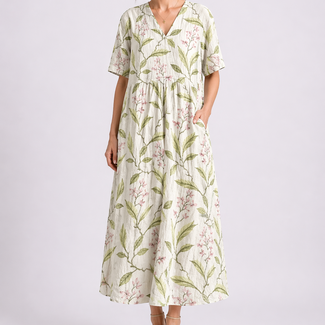 Floral White - Model wearing a woven floral V-neck midaxi dress with short sleeves and side pockets against a plain grey background.