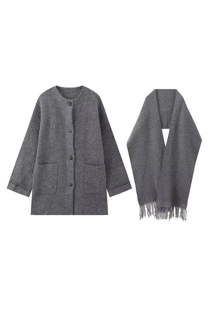 Grey - A woman wearing a thick, taupe oversized longline winter coat featuring a built-in scarf neckline, dark button closures, and large patch pockets.