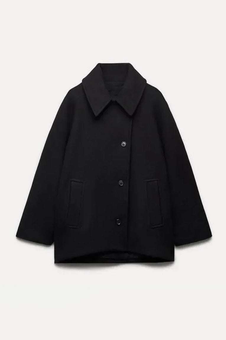 Khaki - A woman wearing a black oversized short coat with drop shoulders and a notched lapel, styled over a grey turtleneck and black shorts for a chic city look.