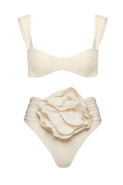 Black - A woman models a structured, off-white two-piece bikini featuring a bandeau top with wide straps and high-waisted, high-cut bottoms adorned with a large, 3D rose appliqué at the waist.