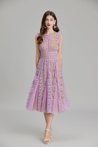 Full-length view of a woman wearing a sleeveless, sheer midi dress in pink and nude, featuring elaborate pink botanical embroidery in vertical panels and a flared tulle skirt.