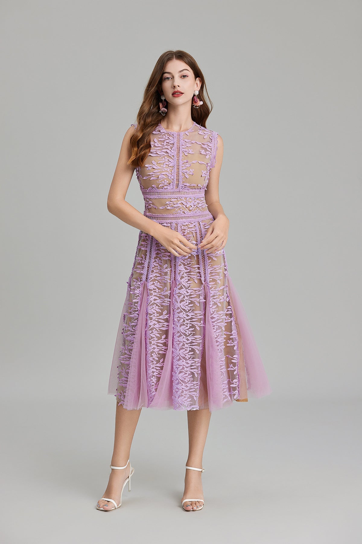 Full-length view of a woman wearing a sleeveless, sheer midi dress in pink and nude, featuring elaborate pink botanical embroidery in vertical panels and a flared tulle skirt.