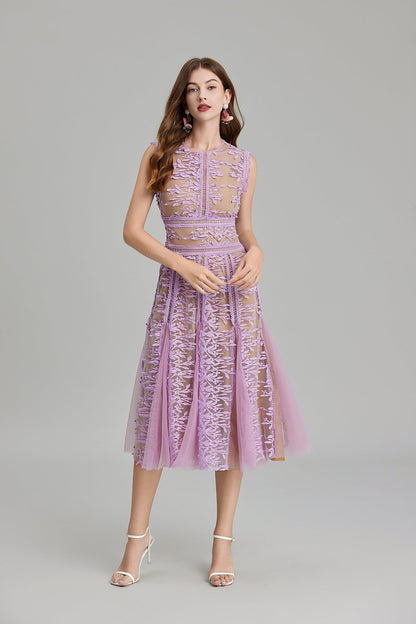 Full-length view of a woman wearing a sleeveless, sheer midi dress in pink and nude, featuring elaborate pink botanical embroidery in vertical panels and a flared tulle skirt.