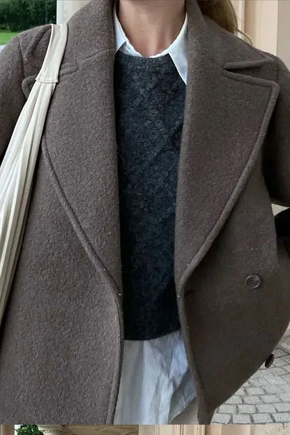Grey - A woman wearing a taupe, short boxy jacket with oversized notch lapels, wide sleeves, and a double-breasted button front, styled over a black top.