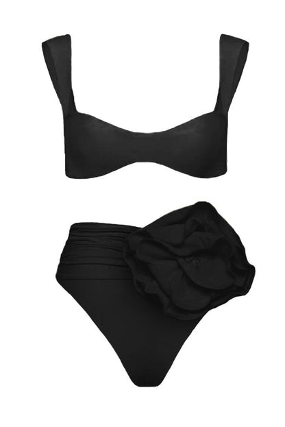 Black - A woman models a structured, off-white two-piece bikini featuring a bandeau top with wide straps and high-waisted, high-cut bottoms adorned with a large, 3D rose appliqué at the waist.