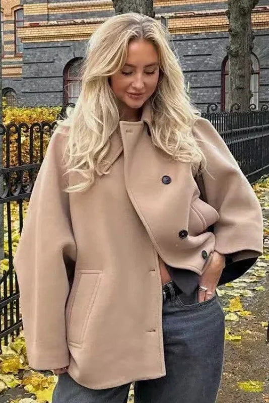 Khaki - A woman wearing a black oversized short coat with drop shoulders and a notched lapel, styled over a grey turtleneck and black shorts for a chic city look.