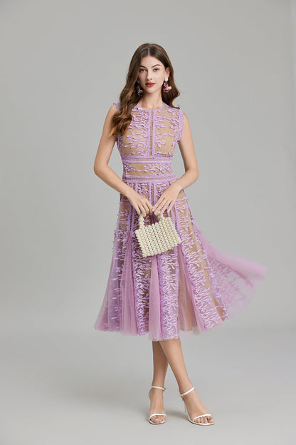 Full-length view of a woman wearing a sleeveless, sheer midi dress in pink and nude, featuring elaborate pink botanical embroidery in vertical panels and a flared tulle skirt.
