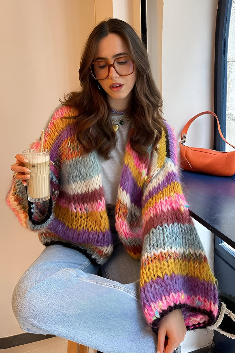 Rainbow - Woman wearing a vibrant, multicoloured striped chunky knit cropped cardigan layered over a white top, standing outdoors.