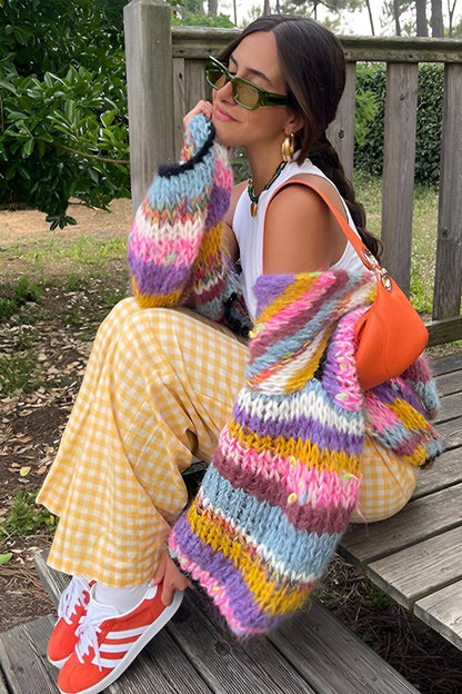 Rainbow - Woman wearing a vibrant, multicoloured striped chunky knit cropped cardigan layered over a white top, standing outdoors.