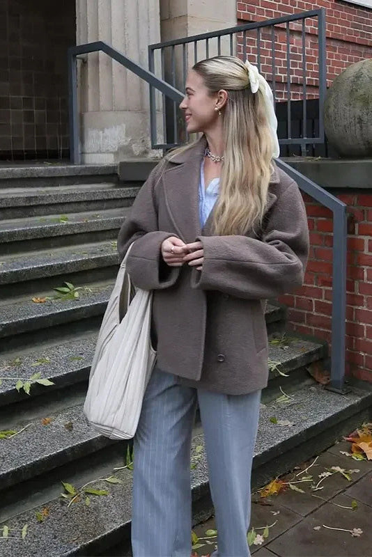 Grey - A woman wearing a taupe, short boxy jacket with oversized notch lapels, wide sleeves, and a double-breasted button front, styled over a black top.