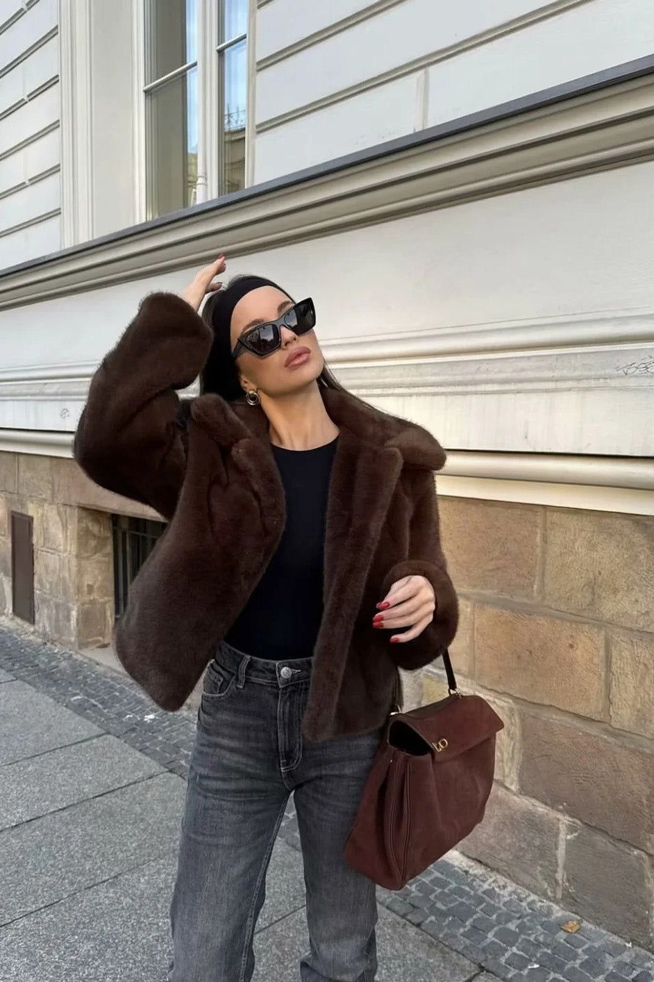 A woman standing outdoors on stone steps wearing a dark brown, plush faux fur cropped jacket with a wide collar, styled with a mini skirt and tall black boots.