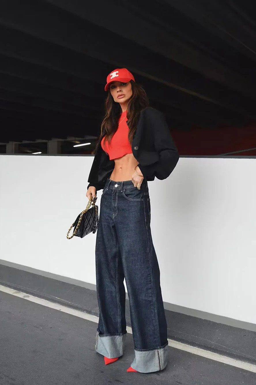 Blue - Woman wearing a dark, structured two-piece outfit consisting of a cropped jacket and high-waisted wide-leg trousers, both featuring prominent contrast turn-up cuffs, walking on a city street at night.