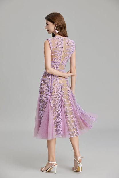 Full-length view of a woman wearing a sleeveless, sheer midi dress in pink and nude, featuring elaborate pink botanical embroidery in vertical panels and a flared tulle skirt.