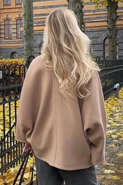 Khaki - A woman wearing a black oversized short coat with drop shoulders and a notched lapel, styled over a grey turtleneck and black shorts for a chic city look.