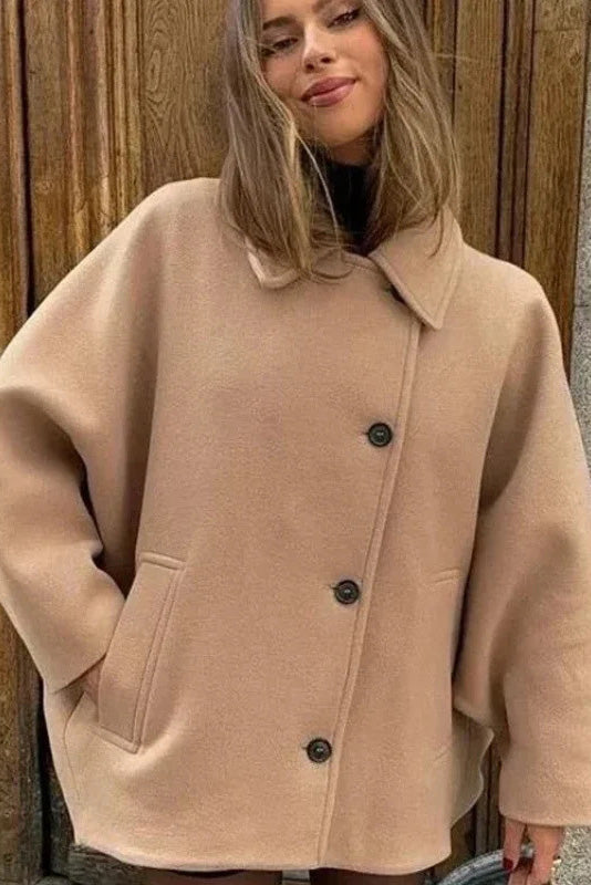 Khaki - A woman wearing a black oversized short coat with drop shoulders and a notched lapel, styled over a grey turtleneck and black shorts for a chic city look.