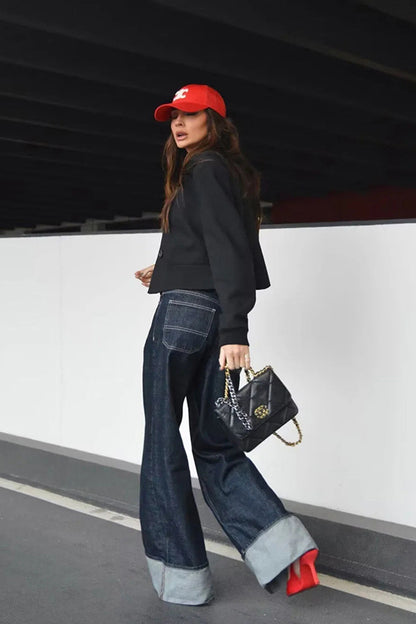 Blue - Woman wearing a dark, structured two-piece outfit consisting of a cropped jacket and high-waisted wide-leg trousers, both featuring prominent contrast turn-up cuffs, walking on a city street at night.