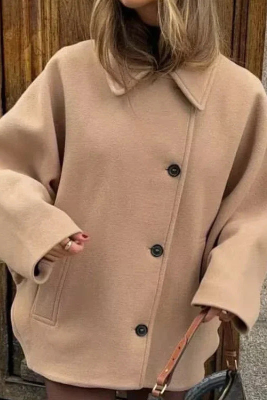 Khaki - A woman wearing a black oversized short coat with drop shoulders and a notched lapel, styled over a grey turtleneck and black shorts for a chic city look.