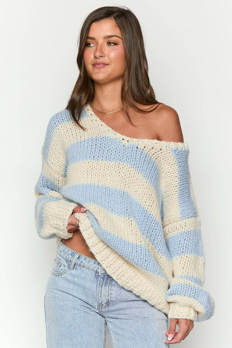 Blue - Woman wearing a chunky knit, slouchy off-shoulder jumper featuring wide horizontal stripes, paired with light wash denim jeans.
