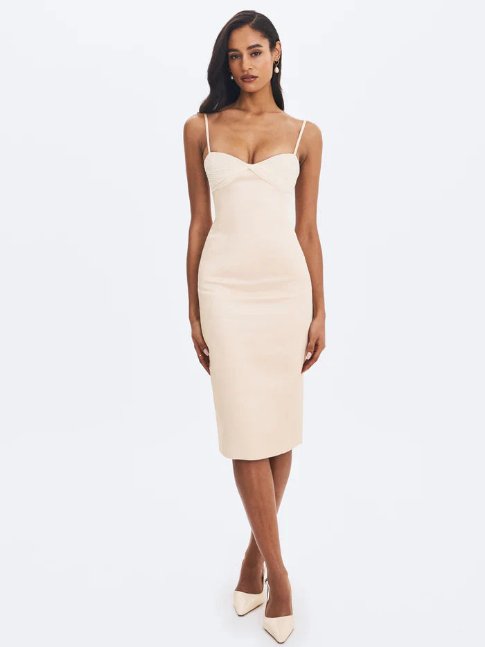 A woman modeling a fitted cream-colored midi dress with spaghetti straps and a ruched sweetheart neckline.