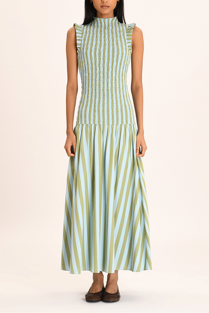 A woman models a sleeveless maxi dress with a high neckline and a fully smocked bodice. The dress features a pattern of vertical light blue and olive green stripes, ruffled shoulder details, and a full A-line skirt.