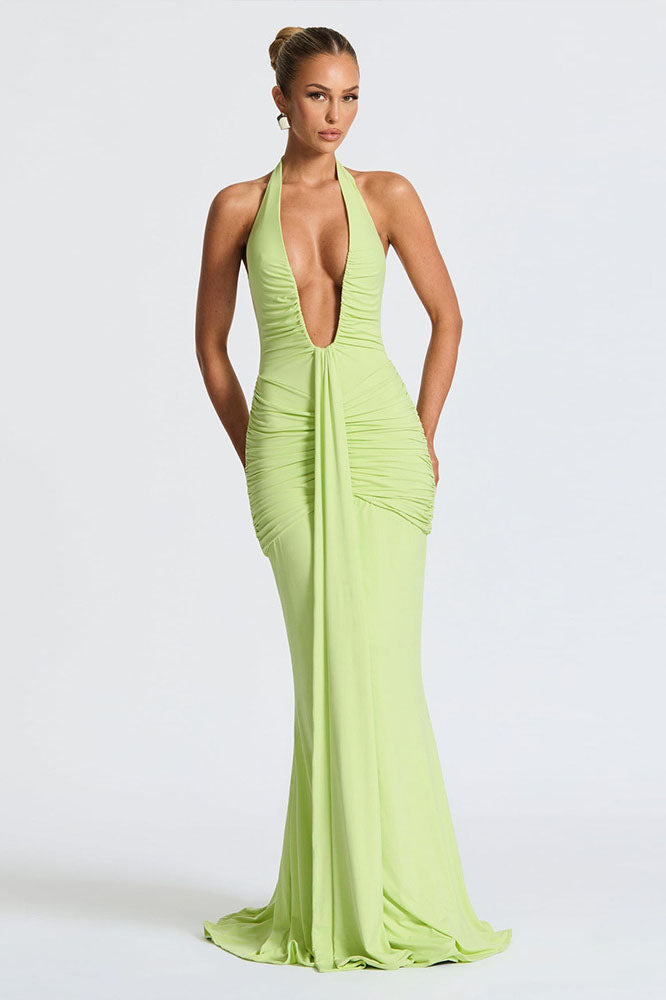Green - A woman models a form-fitting, deep red halterneck maxi dress with a plunging neckline and extensive ruching, standing elegantly in a formal garden setting.