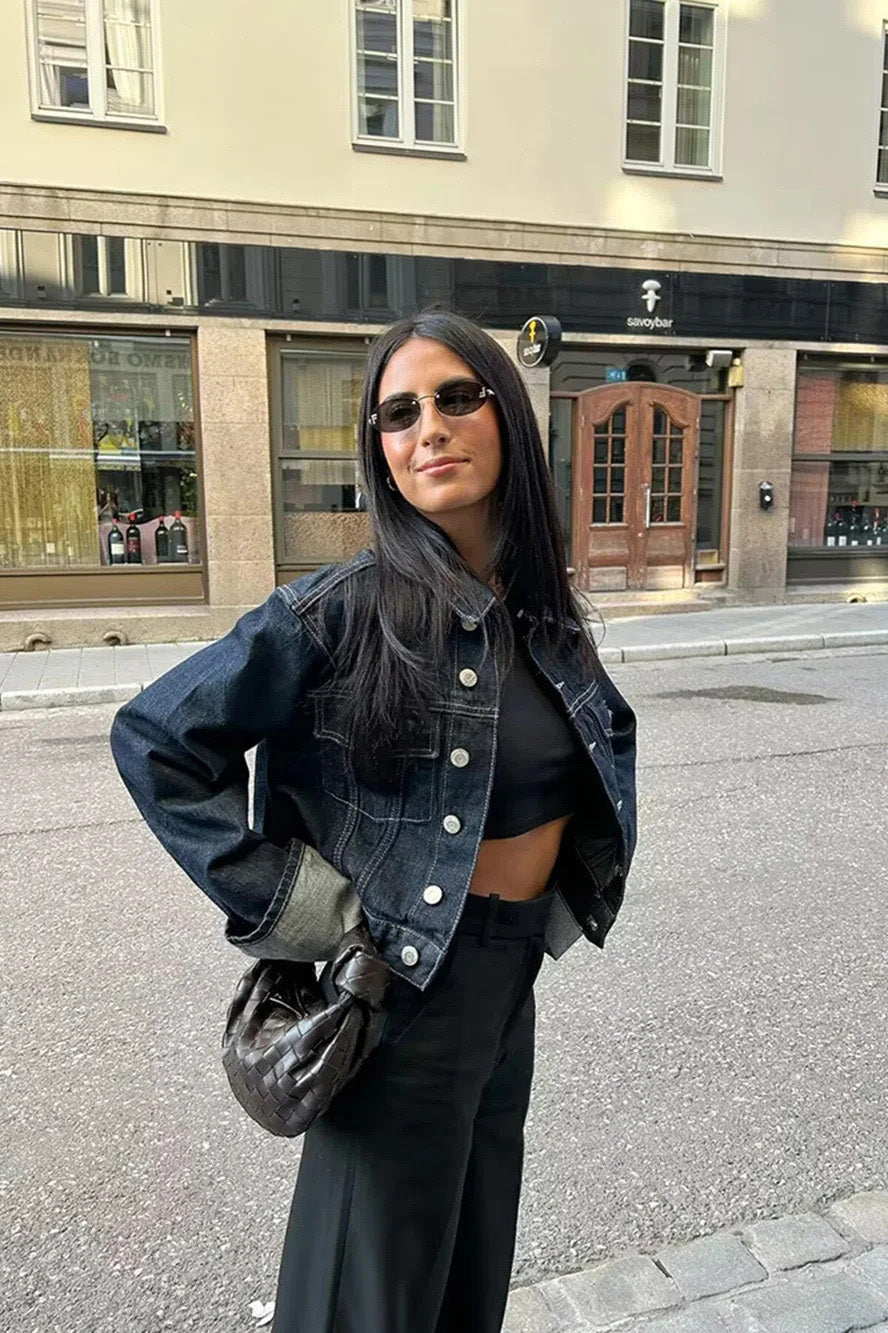 Blue - Woman wearing a dark, structured two-piece outfit consisting of a cropped jacket and high-waisted wide-leg trousers, both featuring prominent contrast turn-up cuffs, walking on a city street at night.