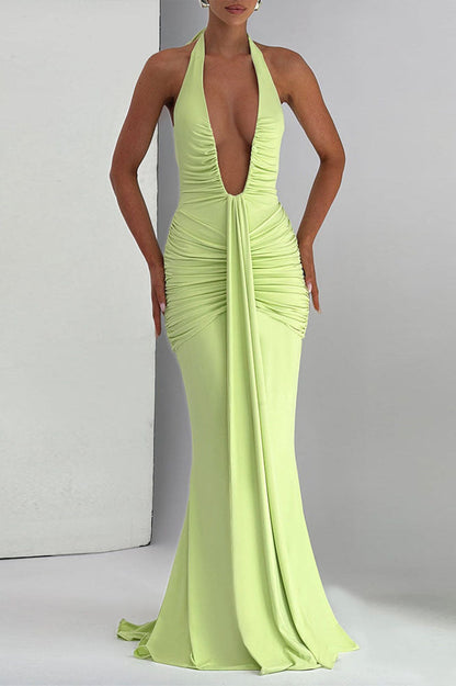 Green - A woman models a form-fitting, deep red halterneck maxi dress with a plunging neckline and extensive ruching, standing elegantly in a formal garden setting.