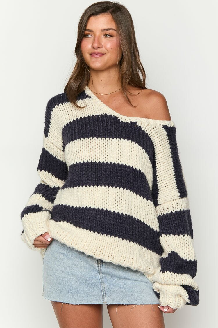 Black - Woman wearing a chunky knit, slouchy off-shoulder jumper featuring wide horizontal stripes, paired with light wash denim jeans.