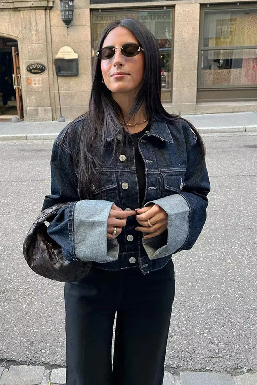 Blue - Woman wearing a dark, structured two-piece outfit consisting of a cropped jacket and high-waisted wide-leg trousers, both featuring prominent contrast turn-up cuffs, walking on a city street at night.