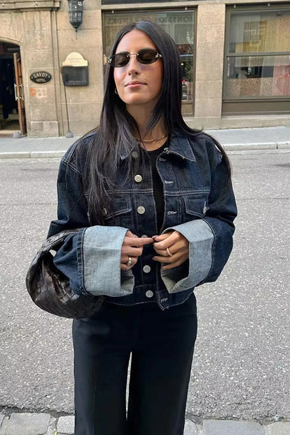 Blue - Woman wearing a dark, structured two-piece outfit consisting of a cropped jacket and high-waisted wide-leg trousers, both featuring prominent contrast turn-up cuffs, walking on a city street at night.