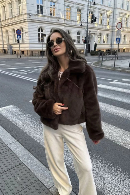 Brown - A woman standing outdoors on stone steps wearing a dark brown, plush faux fur cropped jacket with a wide collar, styled with a mini skirt and tall black boots.