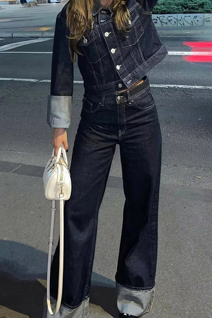 Blue - Woman wearing a dark, structured two-piece outfit consisting of a cropped jacket and high-waisted wide-leg trousers, both featuring prominent contrast turn-up cuffs, walking on a city street at night.