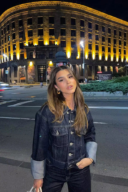 Blue - Woman wearing a dark, structured two-piece outfit consisting of a cropped jacket and high-waisted wide-leg trousers, both featuring prominent contrast turn-up cuffs, walking on a city street at night.