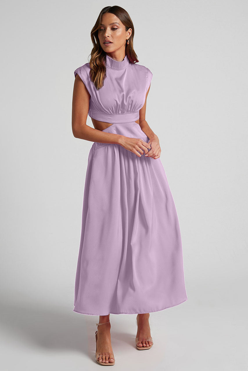 A woman walks outdoors in a pale yellow midi dress, its full skirt flowing around her. The dress features a high funnel neck, cap sleeves, and cutouts at the waist.
