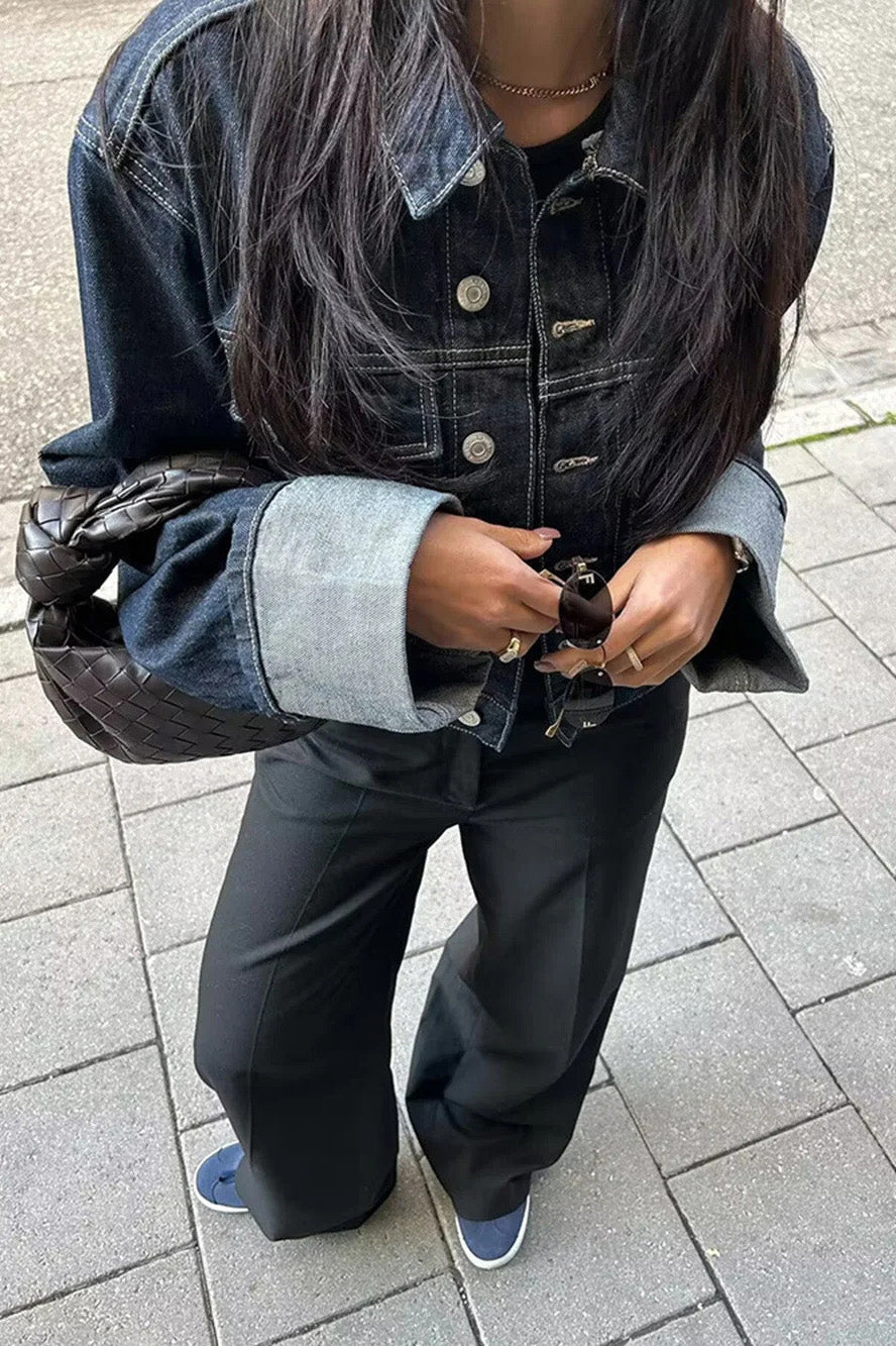 Blue - Woman wearing a dark, structured two-piece outfit consisting of a cropped jacket and high-waisted wide-leg trousers, both featuring prominent contrast turn-up cuffs, walking on a city street at night.
