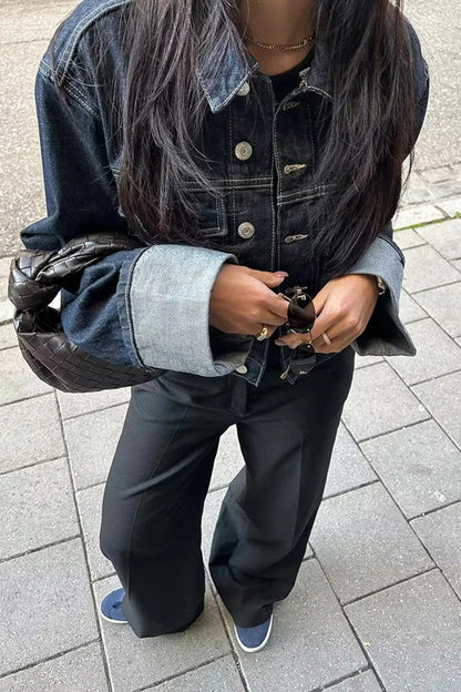 Blue - Woman wearing a dark, structured two-piece outfit consisting of a cropped jacket and high-waisted wide-leg trousers, both featuring prominent contrast turn-up cuffs, walking on a city street at night.