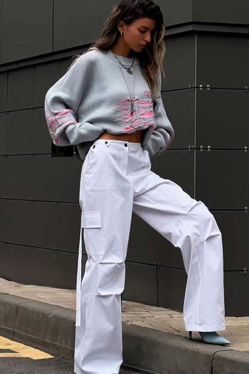 Grey - Model wearing a women's oversized black knit jumper featuring heavy distressed laddering and cut-outs, styled with a white mini skirt.