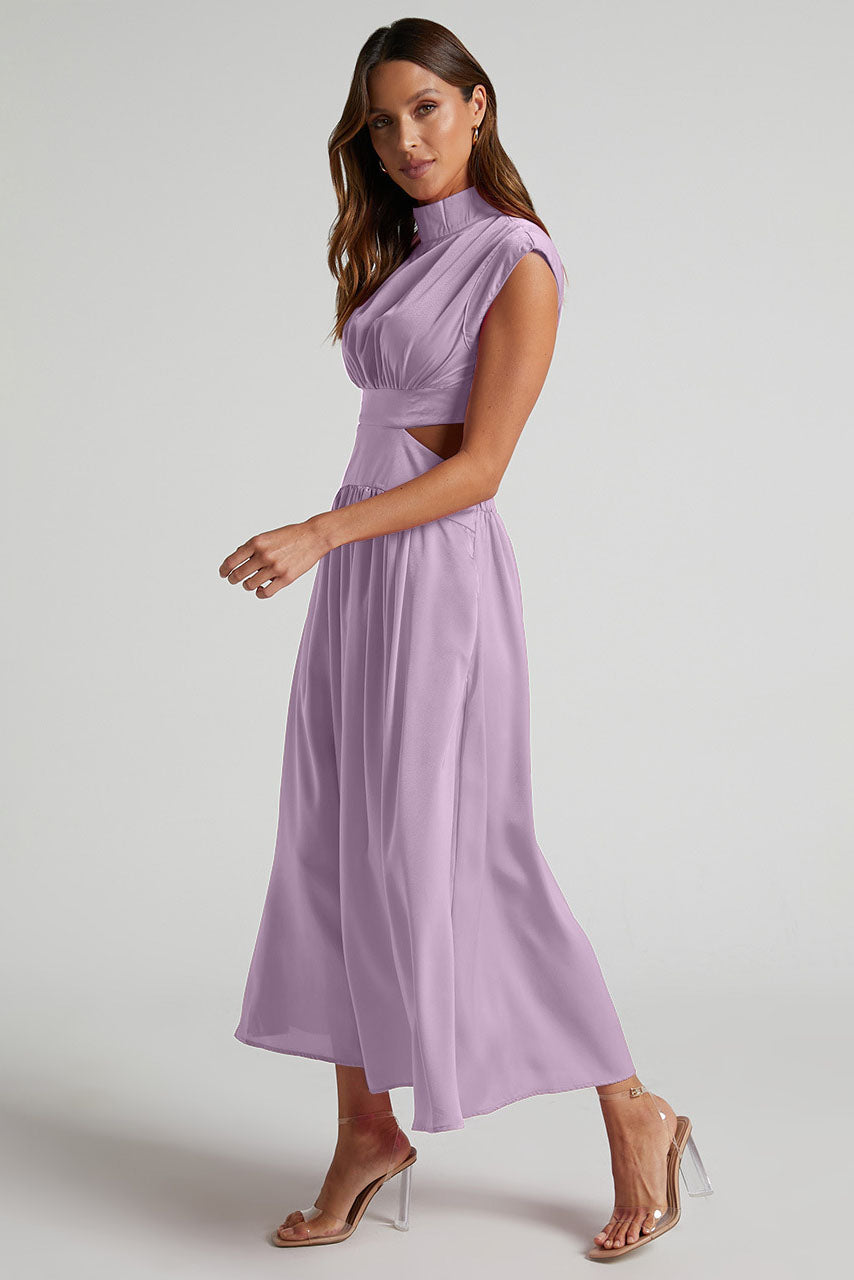A woman walks outdoors in a pale yellow midi dress, its full skirt flowing around her. The dress features a high funnel neck, cap sleeves, and cutouts at the waist.