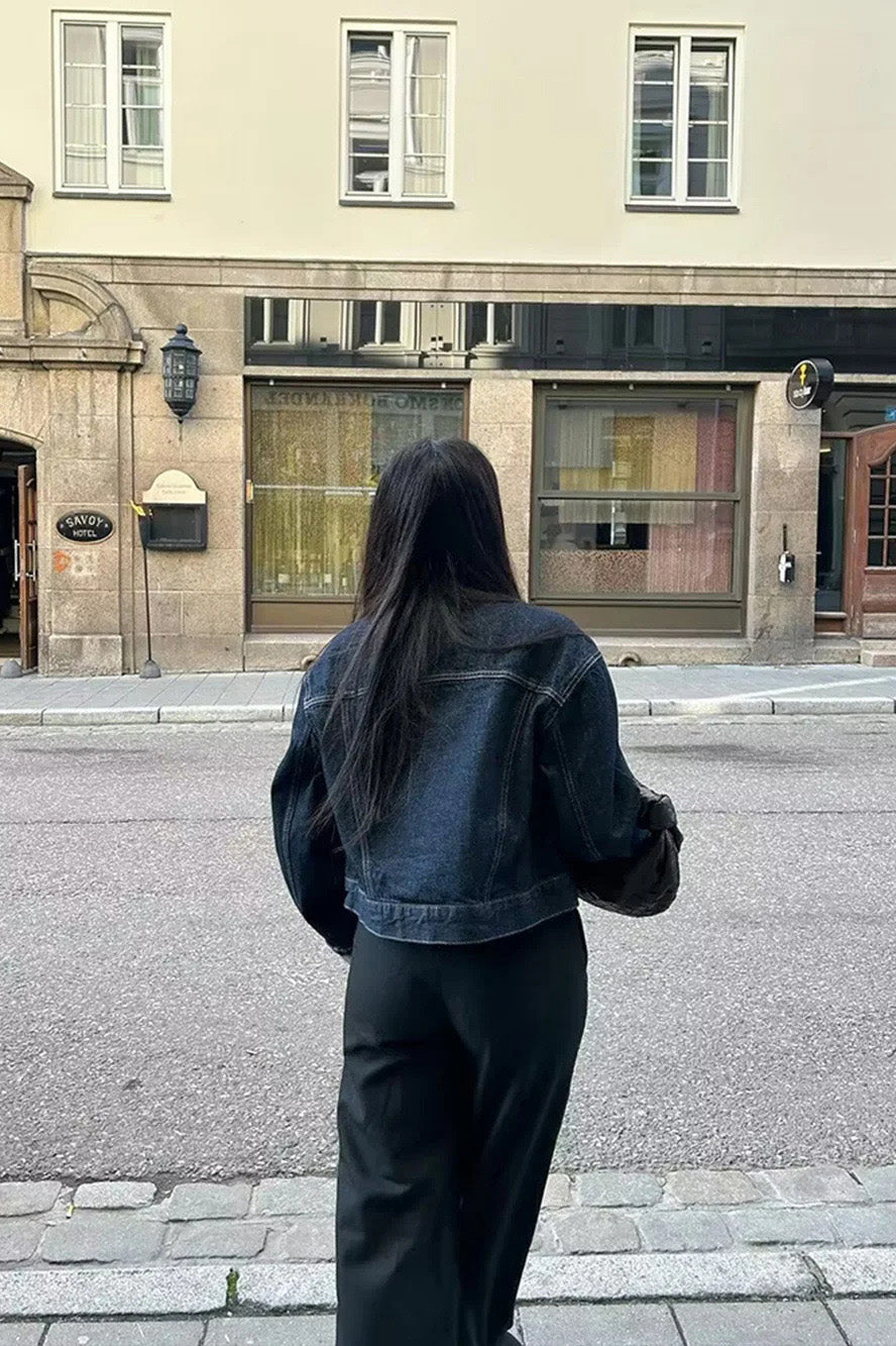 Blue - Woman wearing a dark, structured two-piece outfit consisting of a cropped jacket and high-waisted wide-leg trousers, both featuring prominent contrast turn-up cuffs, walking on a city street at night.