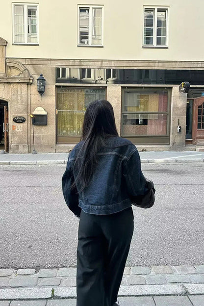 Blue - Woman wearing a dark, structured two-piece outfit consisting of a cropped jacket and high-waisted wide-leg trousers, both featuring prominent contrast turn-up cuffs, walking on a city street at night.