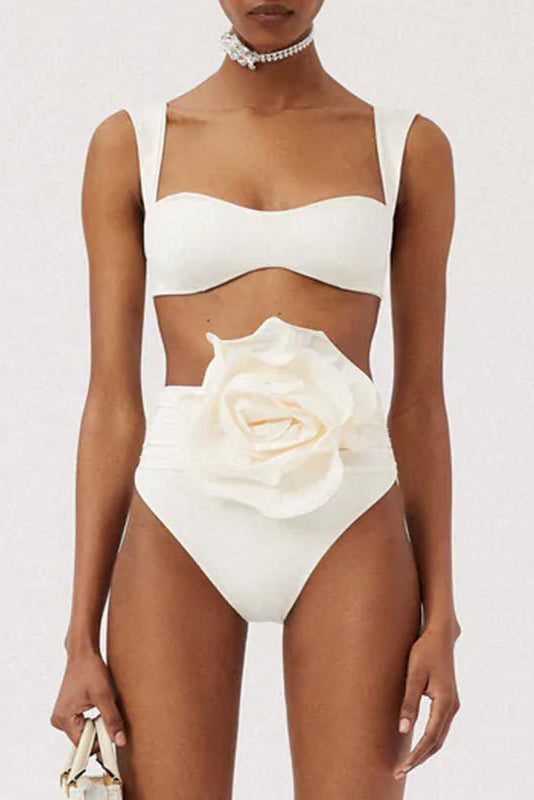 White - A woman models a structured, off-white two-piece bikini featuring a bandeau top with wide straps and high-waisted, high-cut bottoms adorned with a large, 3D rose appliqué at the waist.