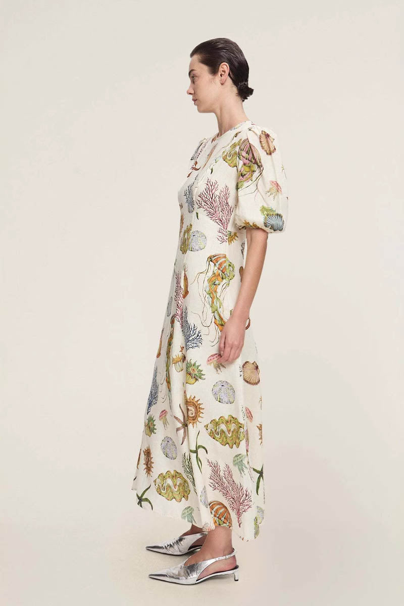 A woman models a short-sleeve, crewneck midi dress with a white background and a colorful, illustrative print of marine life including jellyfish, coral, and seashells.