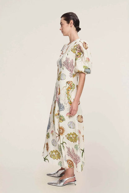 A woman models a short-sleeve, crewneck midi dress with a white background and a colorful, illustrative print of marine life including jellyfish, coral, and seashells.
