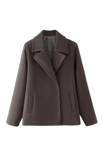 Grey - A woman wearing a taupe, short boxy jacket with oversized notch lapels, wide sleeves, and a double-breasted button front, styled over a black top.