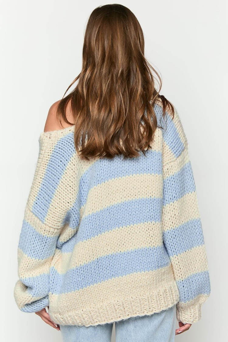 Blue - Woman wearing a chunky knit, slouchy off-shoulder jumper featuring wide horizontal stripes, paired with light wash denim jeans.